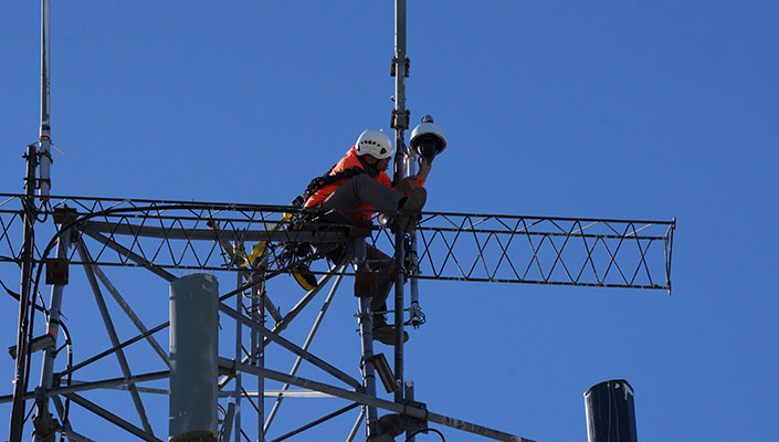 An ALERTCalifornia technician is strapped into safety gear high on a tower to install a new camera